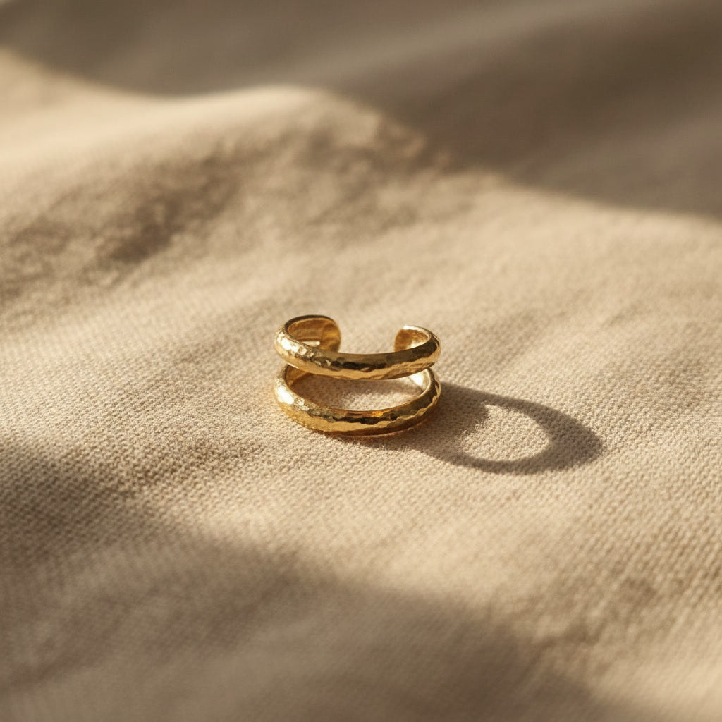 Gehämmerter goldener Ear Cuff Martellato seitlich auf beigem Leinen.