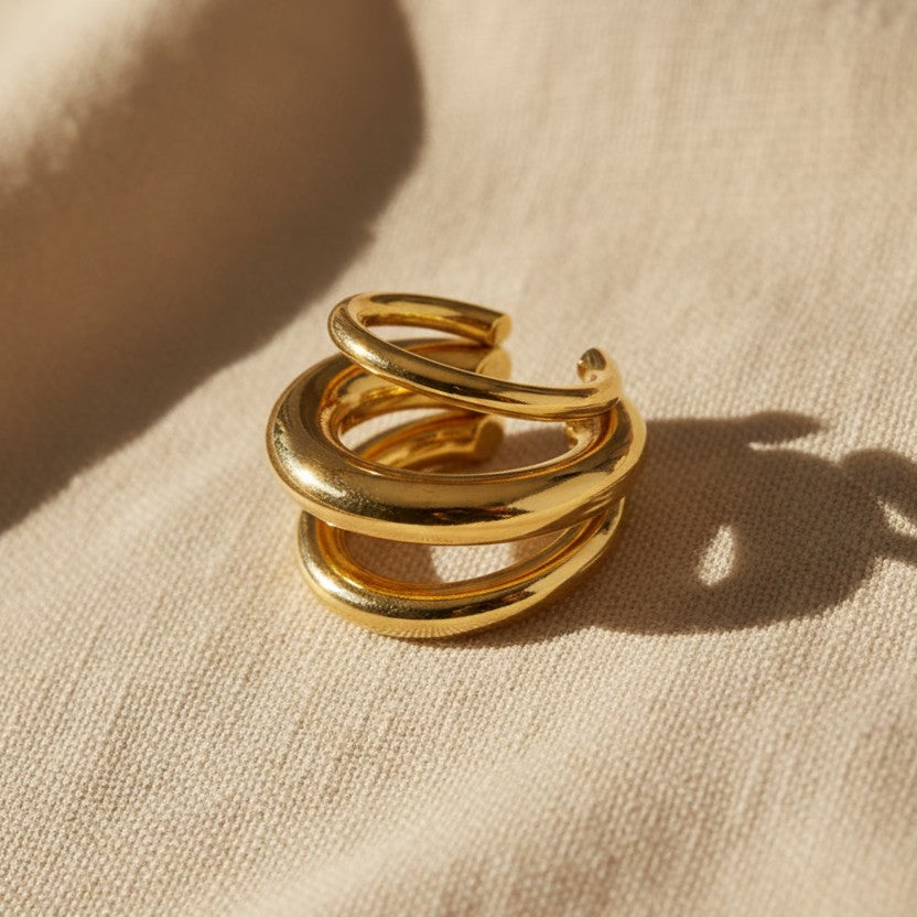 Goldener Ear Cuff Spira mit drei geschwungenen Reihen auf hellem Leinenstoff.