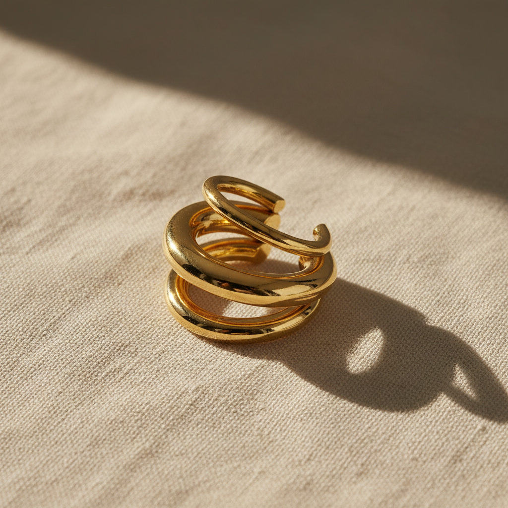 Dreireihiger goldener Ear Cuff Spira auf hellem Stoff mit natürlichem Sonnenlicht und Schatten.