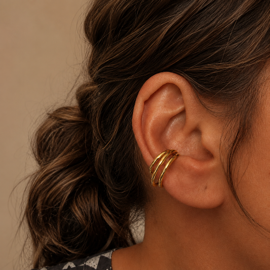 Goldener Ear Cuff Vela aus 304 Edelstahl mit 18K Gold PVD-Beschichtung am Ohr eines Models getragen, kombiniert mit einem kleinen goldenen Ohrstecker.