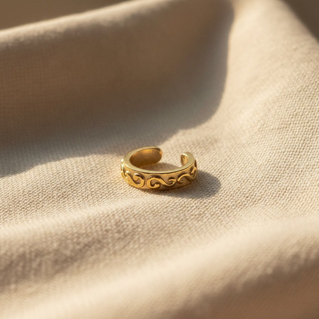 Goldfarbener Arabesco Ear Cuff mit dekorativem Wellen- und Reliefmuster auf warmem Leinenstoff.