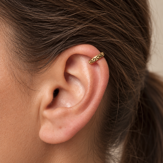 Arabesco Ear Cuff in Gold mit ornamentalem Reliefmuster in seitlicher Ansicht auf beigefarbenem Leinen.