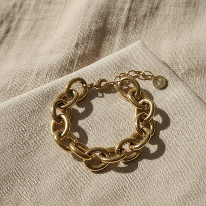 Goldfarbenes Bella Chunky Armband auf beigem Leinenstoff im warmen Sonnenlicht.