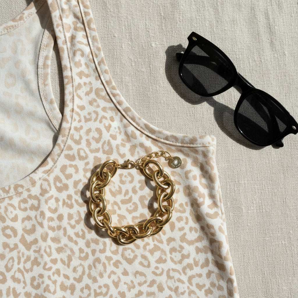 Goldfarbenes Bella Chunky Armband auf gemustertem Top neben schwarzer Sonnenbrille.