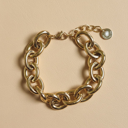 Goldfarbenes Bella Chunky Armband mit großen glänzenden Gliedern auf warmem beigem Hintergrund.