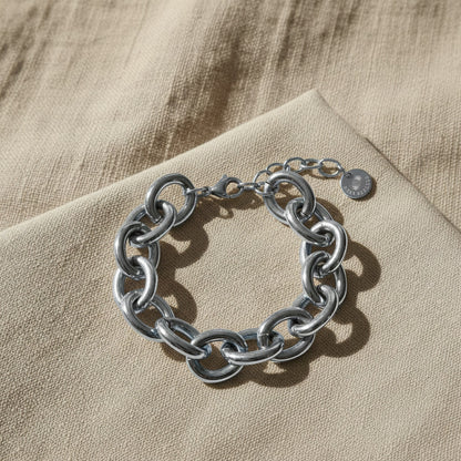 Silberfarbenes Bella Chunky Armband auf beigem Leinenstoff im warmen Sonnenlicht.
