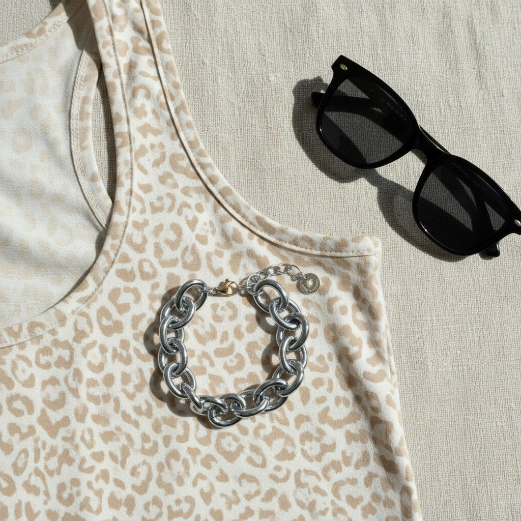 Silberfarbenes Bella Chunky Armband auf gemustertem Top neben schwarzer Sonnenbrille.