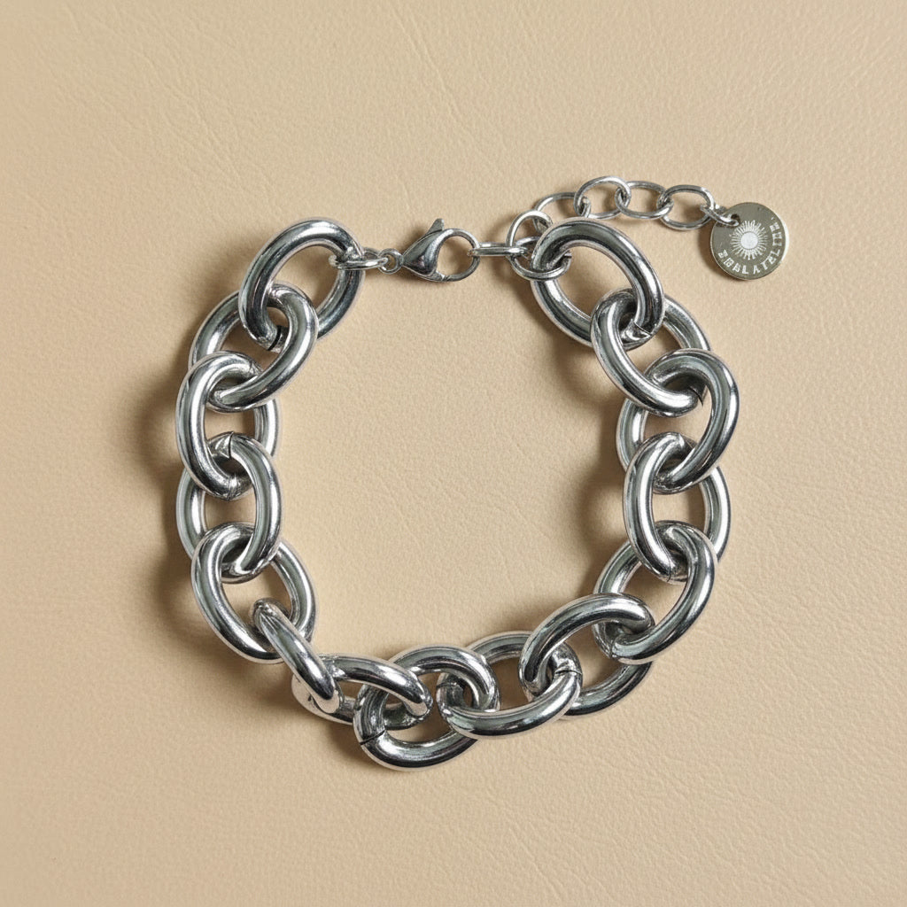 Silberfarbenes Bella Chunky Armband mit großen glänzenden Gliedern auf warmem beigem Hintergrund.