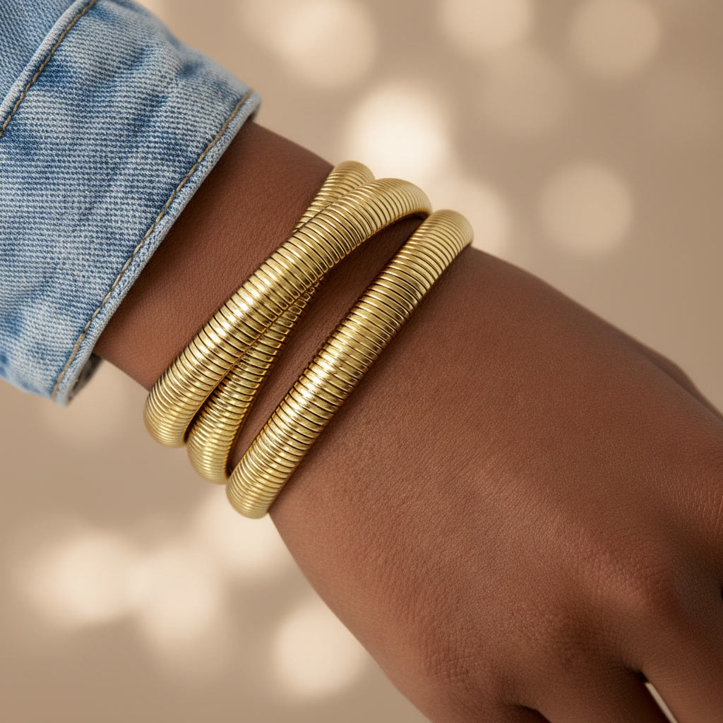 Goldfarbenes Spirale d’Oro Armband mit dreifacher Wickel-Optik, getragen am Handgelenk zu Jeans.