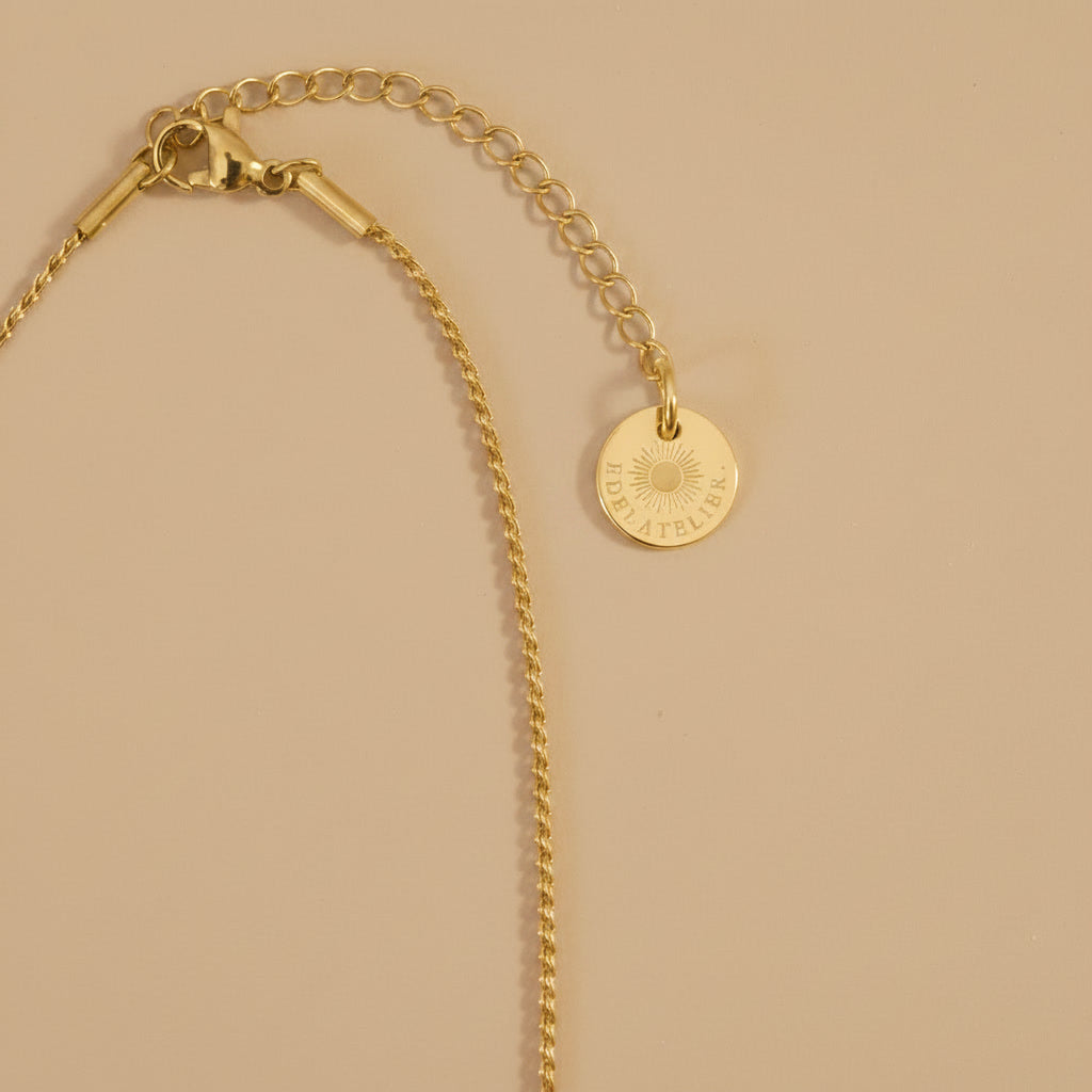 Detailaufnahme der goldfarbenen Cuore Halskette mit kleinem Herzanhänger auf warmem beigem Hintergrund.