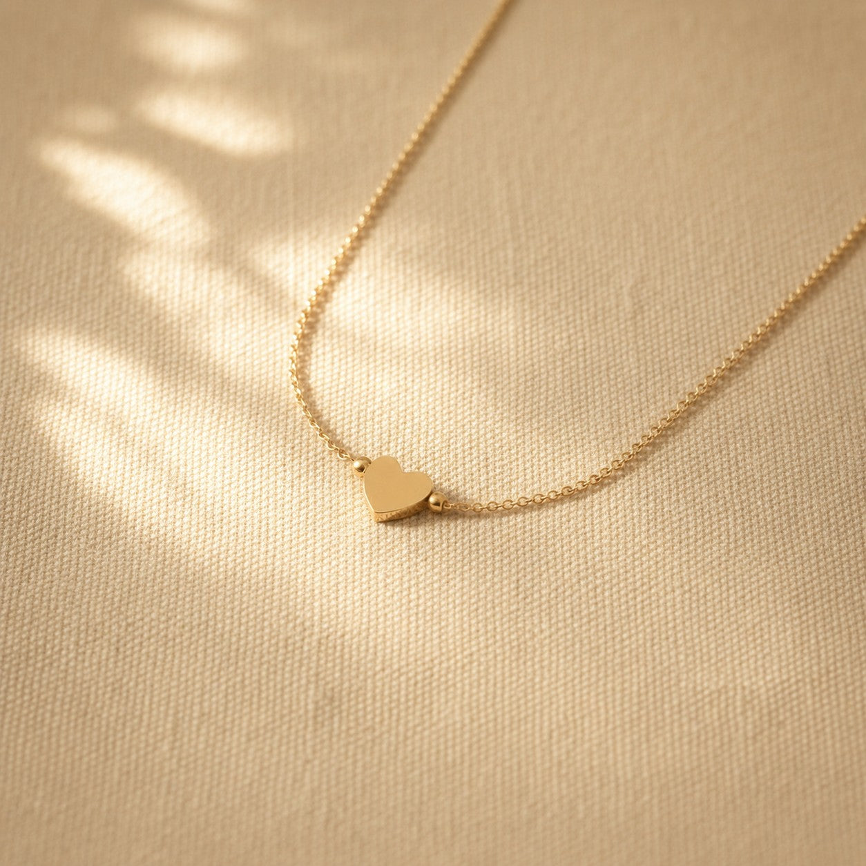 Cuore Halskette goldfarben mit Herzanhänger auf warmem Leinenstoff im Sonnenlicht