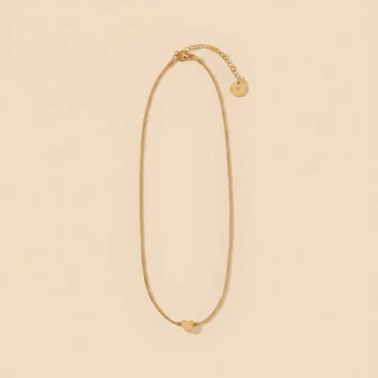 Goldfarbene Cuore Halskette mit kleinem Herzanhänger auf warmem beigem Hintergrund.