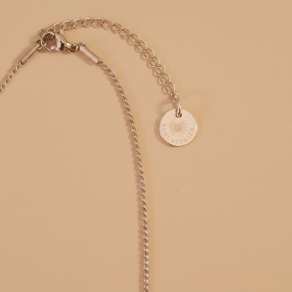 Detailaufnahme der silberfarbenen Cuore Halskette mit Verlängerungskette und EDELATELIER.-Logoplättchen.