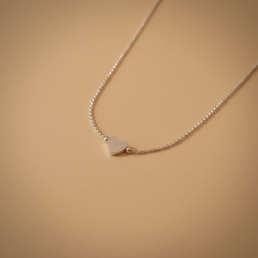 Detailaufnahme der silberfarbenen Cuore Halskette mit kleinem Herzanhänger auf warmem beigem Hintergrund.