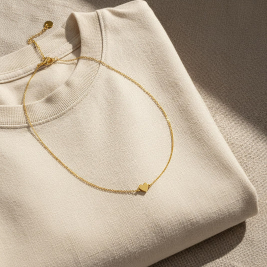 Goldfarbene Herz-Halskette auf cremefarbenem Pullover im warmen Sonnenlicht.