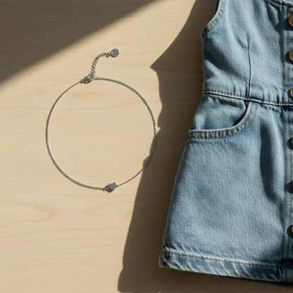 Silberfarbene Cuore Herz-Halskette neben Jeansstoff im sommerlichen Look.