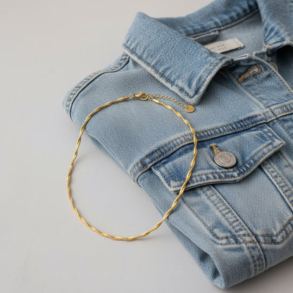 Goldfarbene Intreccia Halskette mit gedrehter Struktur neben hellblauer Jeansjacke.