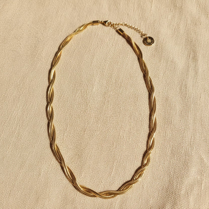 Intreccia Halskette aus 14 Karat vergoldetem Edelstahl auf hellem Leinenstoff mit sanftem Sonnenlicht.
