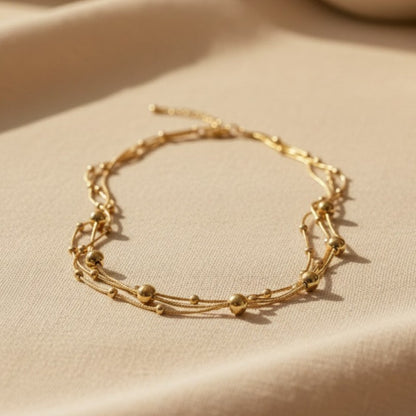 Mehrlagige Piccola Perla Halskette aus goldfarbenem Edelstahl mit Kugeldetails auf warmem Leinenstoff.
