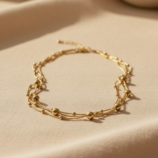 Mehrlagige Piccola Perla Halskette aus goldfarbenem Edelstahl mit Kugeldetails auf warmem Leinenstoff.