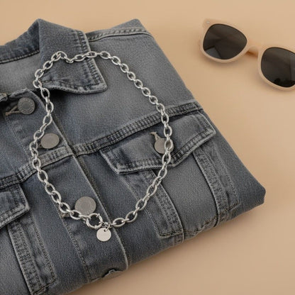 Silberfarbene Maglia Halskette auf gefalteter Jeansjacke mit Sonnenbrille im lässigen Sommerlook.