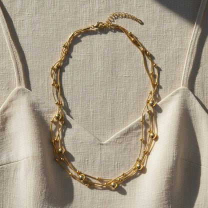 Mehrreihige goldfarbene Halskette mit Kugeldetails auf hellem Leinen-Top im warmen Sonnenlicht.