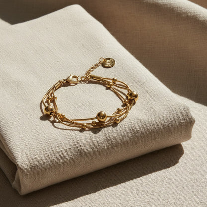 Goldfarbenes Piccola Perla Armband mit feinen Kugeldetails auf gefaltetem beigem Leinenstoff im warmen Sonnenlicht.