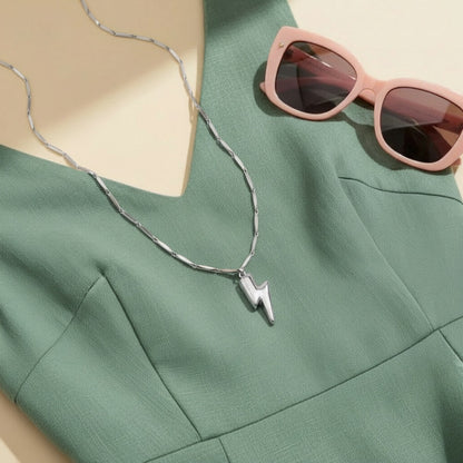 Silberfarbene Saetta Halskette mit Blitzanhänger auf mintgrünem Kleid, kombiniert mit rosafarbener Sonnenbrille.