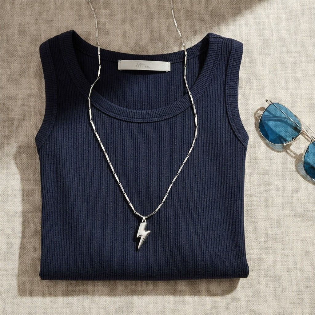 Silberfarbene Saetta Blitz-Halskette auf dunkelblauem Top mit Sonnenbrille im sommerlichen Flatlay.