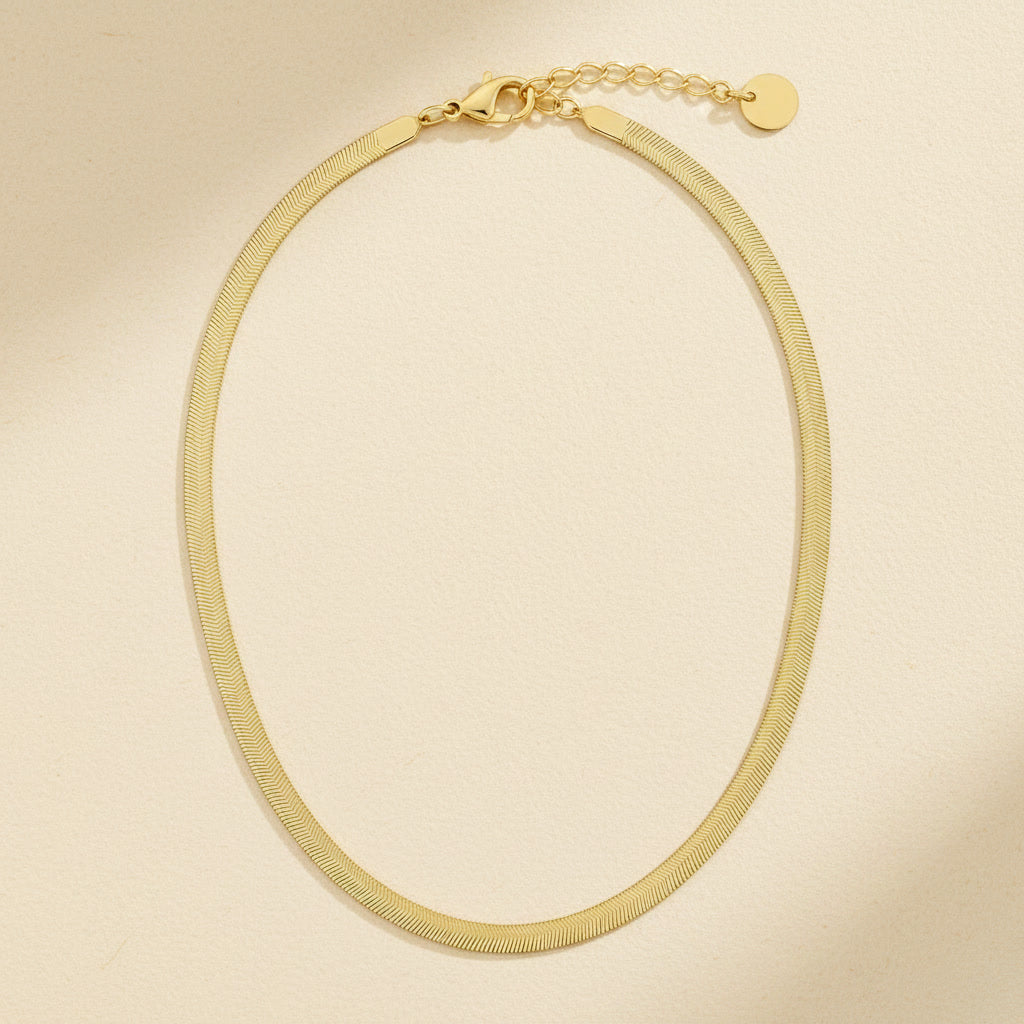 Goldfarbene Serena Halskette mit flacher Struktur, Karabiner und Verlängerungskette auf cremefarbenem Hintergrund.