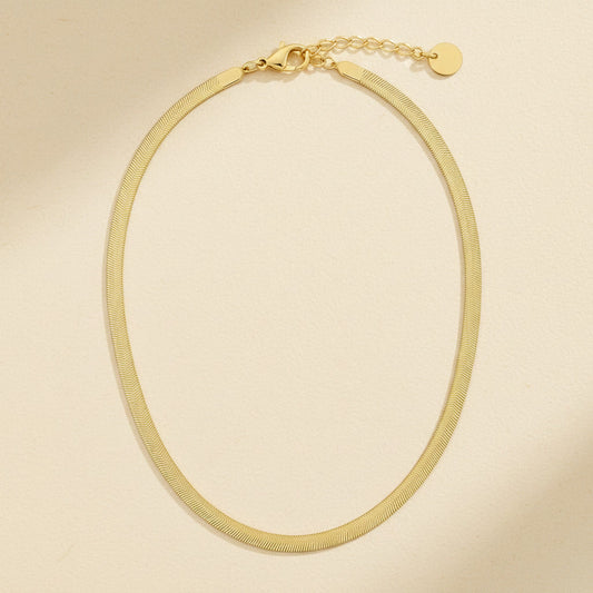 Goldfarbene Serena Halskette mit flacher Struktur, Karabiner und Verlängerungskette auf cremefarbenem Hintergrund.