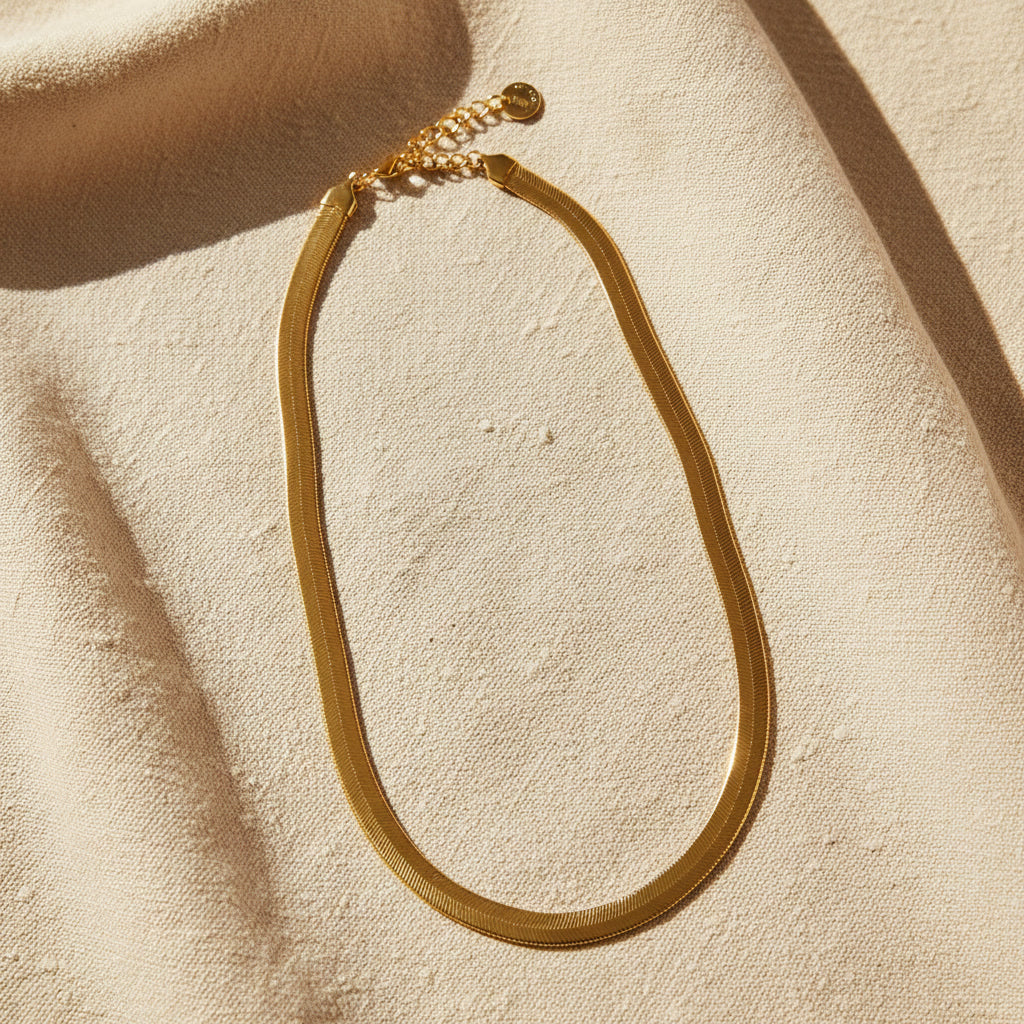 Serena Schlangenkette goldfarben auf hellem Leinen mit warmem Licht und EDELATELIER-Logoplättchen.