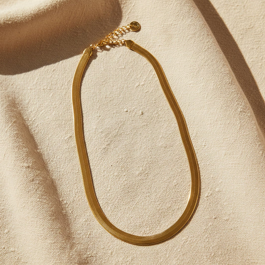 Serena Schlangenkette goldfarben auf hellem Leinen mit warmem Licht und EDELATELIER-Logoplättchen.