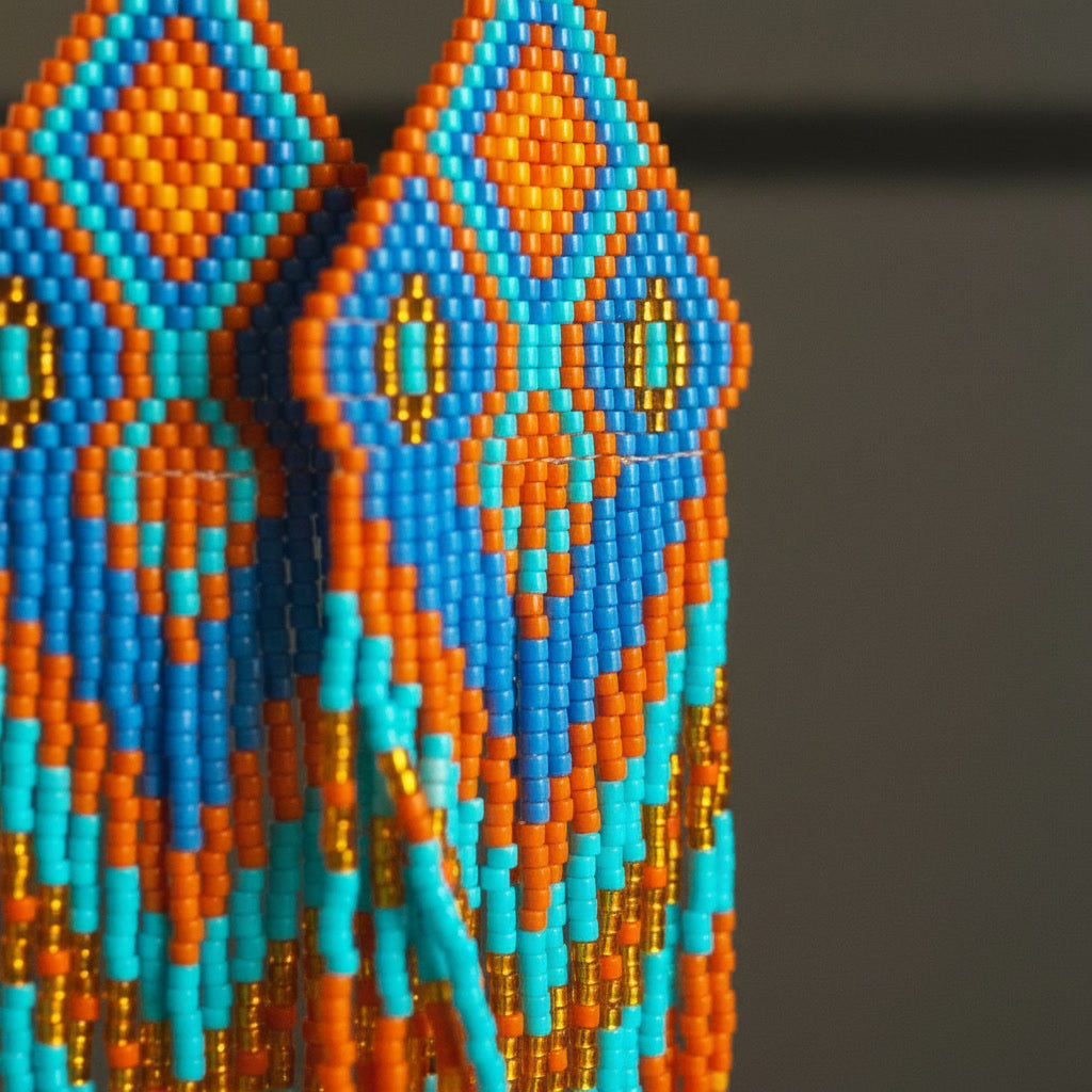 Detaillierte Makroaufnahme des handgewebten Rautenmusters der Ohrringe Fiamma Azzurra von EDELATELIER. Das präzise geometrische Design aus hochwertigen Miyuki-Perlen vereint lebendige Komplementärfarben mit edlen Goldakzenten.Von der Seite aus fotografiert. 