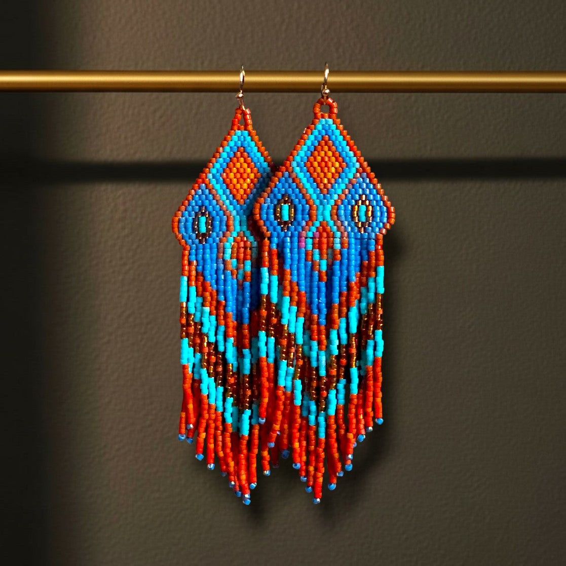 Ein Paar handgefertigte Statement-Ohrringe Modell Fiamma Azzurra von EDELATELIER, präsentiert an einer goldenen Stange. Die 10 cm langen Ohrringe zeigen ein leuchtendes Muster in kräftigem Orange und hellem Türkis, kombiniert mit tiefblauen Akzenten und goldenen Details.
