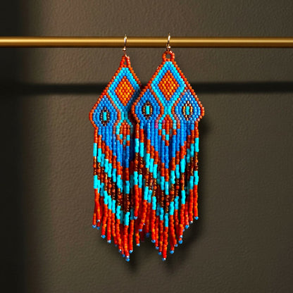 Ein Paar handgefertigte Statement-Ohrringe Modell Fiamma Azzurra von EDELATELIER, präsentiert an einer goldenen Stange. Die 10 cm langen Ohrringe zeigen ein leuchtendes Muster in kräftigem Orange und hellem Türkis, kombiniert mit tiefblauen Akzenten und goldenen Details.