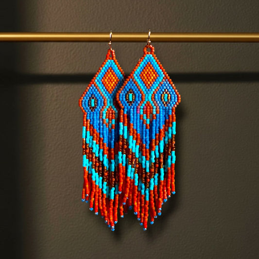 Ein Paar handgefertigte Statement-Ohrringe Modell Fiamma Azzurra von EDELATELIER, präsentiert an einer goldenen Stange. Die 10 cm langen Ohrringe zeigen ein leuchtendes Muster in kräftigem Orange und hellem Türkis, kombiniert mit tiefblauen Akzenten und goldenen Details.