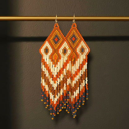Ein Paar handgefertigte Statement-Ohrringe Modell Fiamma di Terra von EDELATELIER, präsentiert an einer goldenen Stange. Die 10 cm langen Ohrringe zeigen ein warmes, erdanaloge Muster in kräftigem Rostrot und Terrakotta, kombiniert mit kontrastreichen Akzenten in Türkis und Creme sowie Golddetails.
