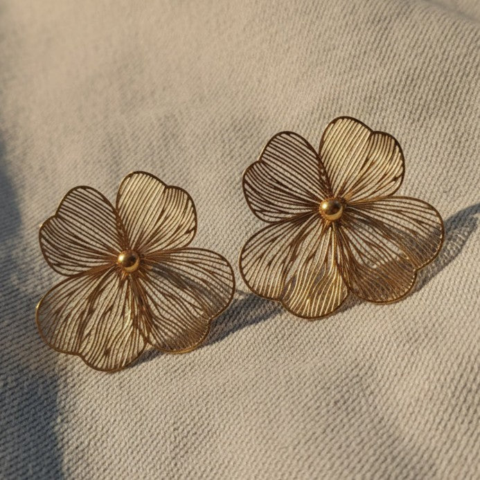 Foglia Blumenohrringe in Goldfarben auf hellem Stoff.