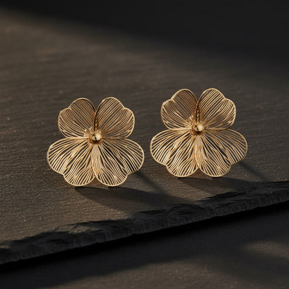 Goldfarbene Foglia Blumenohrringe auf dunklem Hintergrund. 