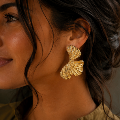 Model trägt goldfarbene Foglia Ohrringe aus Edelstahl in Blattform.