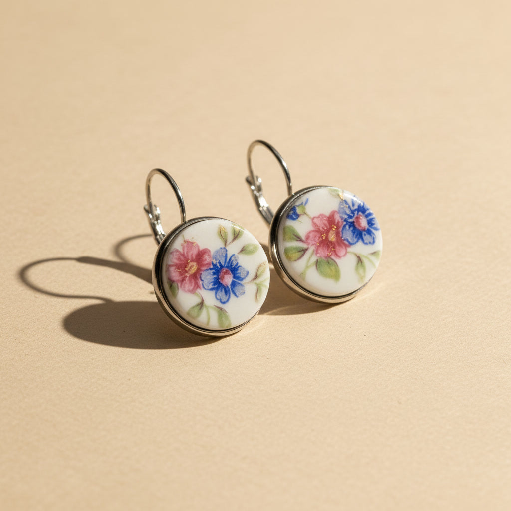 Handgefertigte Porzellanohrringe mit rosa und blauem Blumenmuster in Seitenansicht auf hellem beigem Hintergrund vom Edelatelier