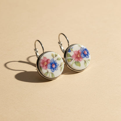 Handgefertigte Porzellanohrringe mit rosa und blauem Blumenmuster in Seitenansicht auf hellem beigem Hintergrund vom Edelatelier