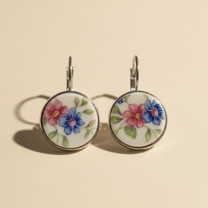 Handgefertigte runde Porzellanohrringe mit rosa und blauem Blumenmuster auf hellem beigem Hintergrund vom Edelatelier
