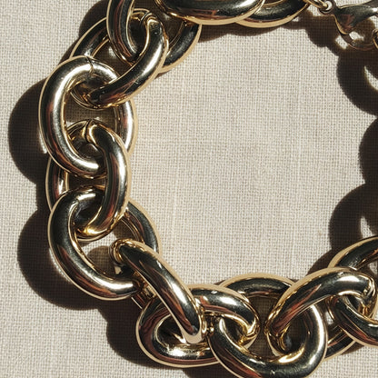 14 Karat vergoldetes Chunky Edelstahlarmband mit großen ovalen Gliedern auf hellem Leinenstoff im warmen Sonnenlicht.