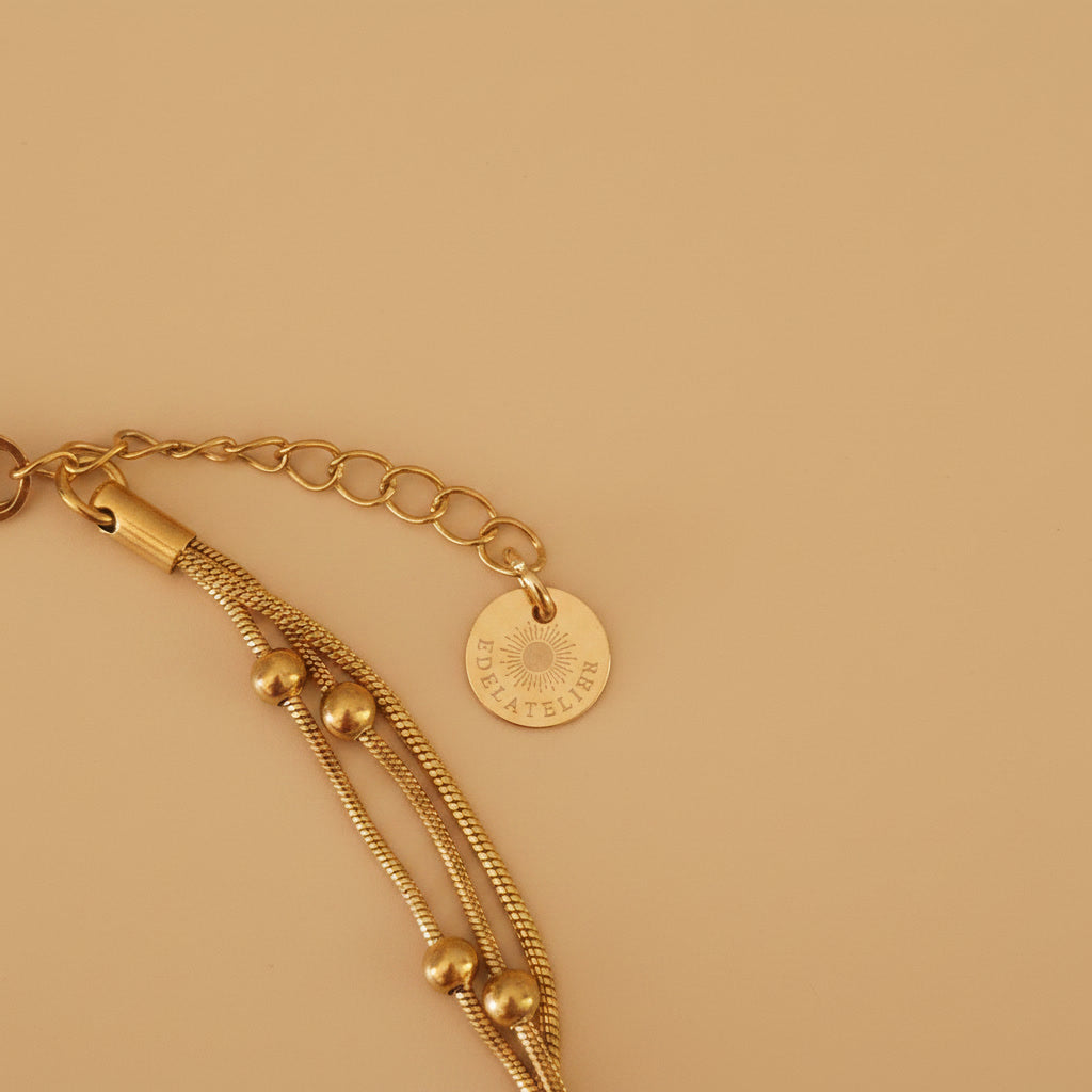 Detailaufnahme der goldfarbenen Piccola Perla Halskette mit Verlängerungskette und EDELATELIER.-Logoplättchen.