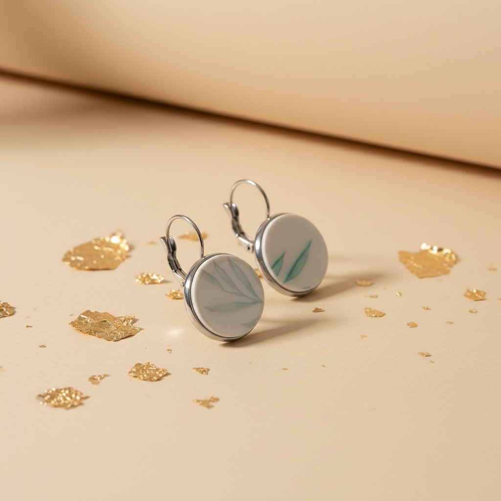 Handgefertigte Porzellanohrringe Glauca mit filigranem, mintgrünem Blattmotiv auf beigem Hintergrund mit Goldflocken von EDELATELIER aus der Seitenperspektive.