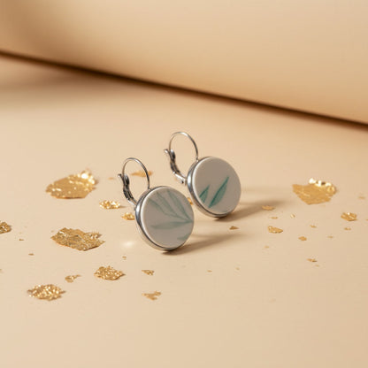 Handgefertigte Porzellanohrringe Glauca mit filigranem, mintgrünem Blattmotiv auf beigem Hintergrund mit Goldflocken von EDELATELIER aus der Seitenperspektive.