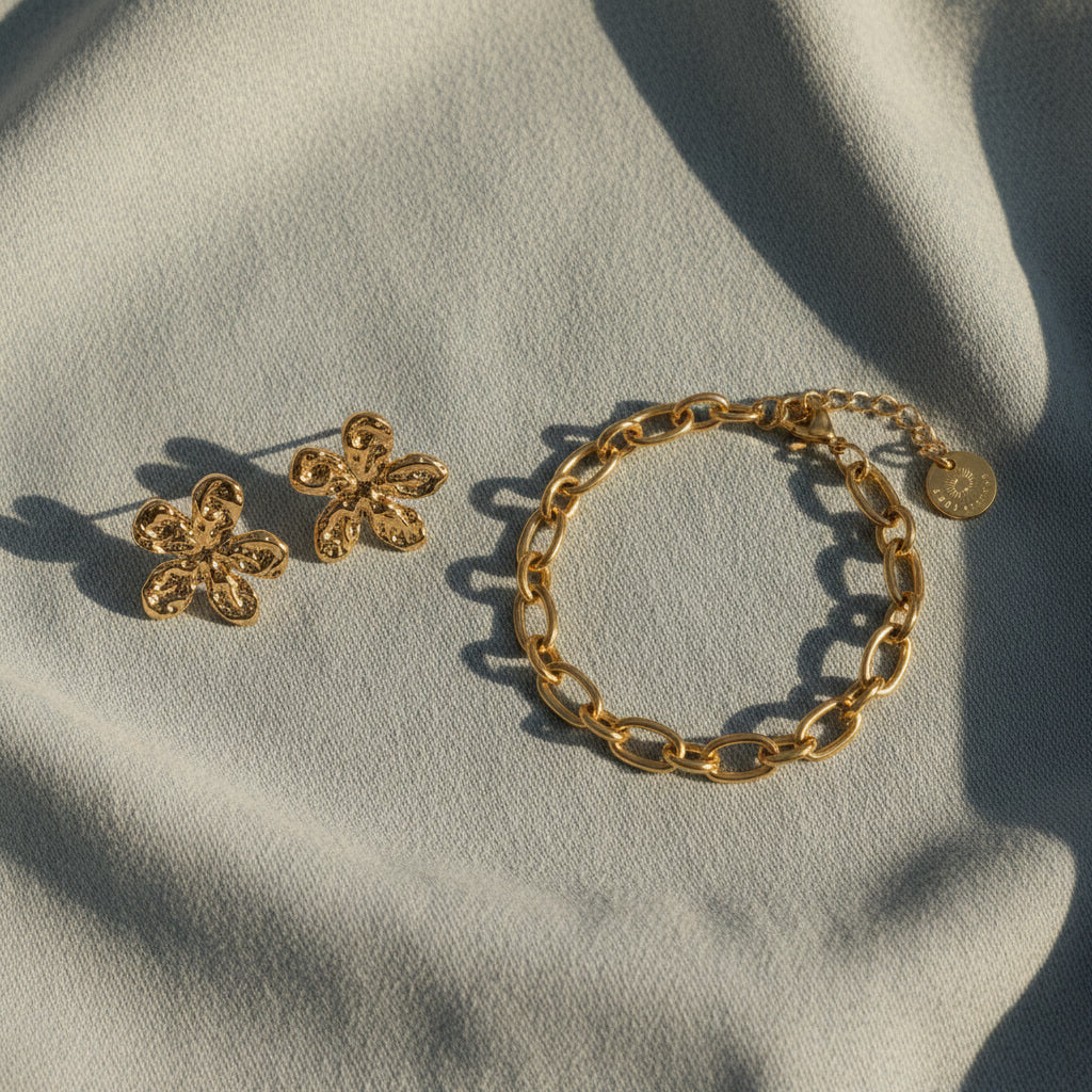 Goldene Blütenohrringe und goldenes Armband auf hellem Stoff.