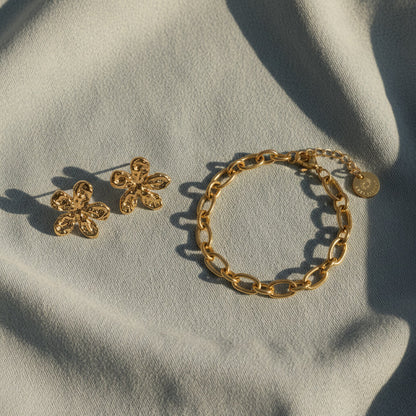 Goldene Blütenohrringe und goldenes Armband auf hellem Stoff.
